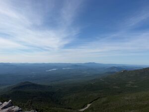 The view from the summit of Whiteface Mountain over forested Adirondack hills, a distant lake, and mountains on the horizon.
